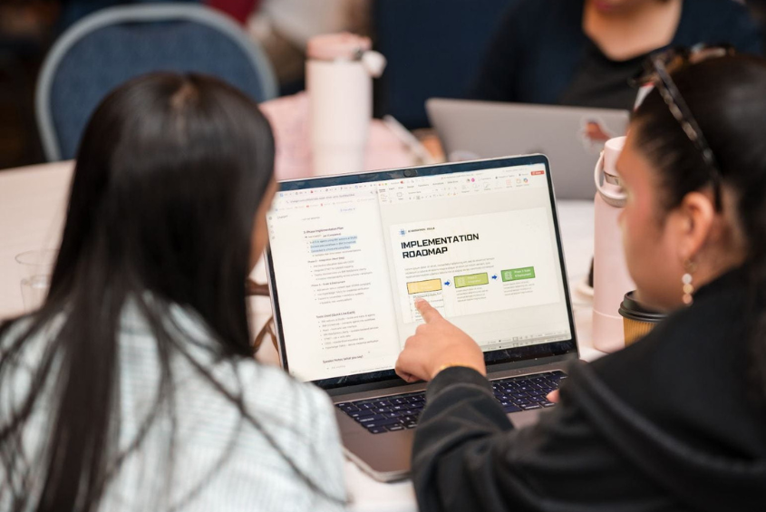 Two people pointing at a laptop screen that says "Implementation Roadmap"